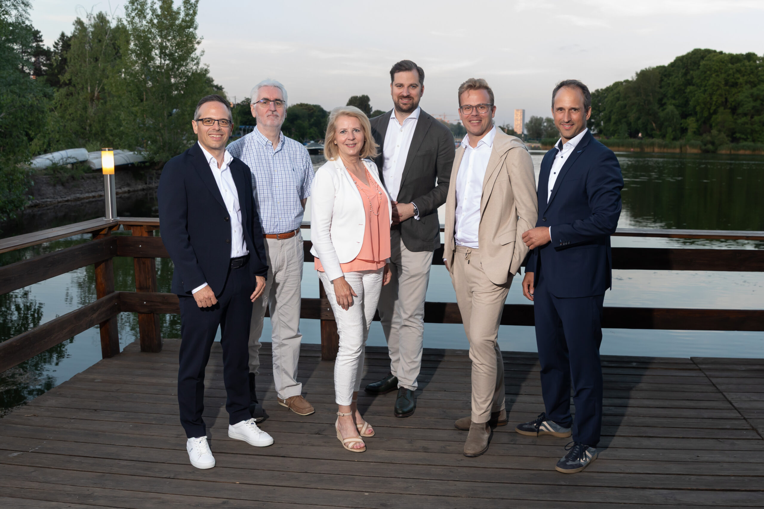 Sechs formal gekleidete Personen stehen im Freien und posieren für ein Pressefoto.