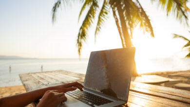 Notebook auf einem Tisch, mit Palme und Meer im Hintergrund