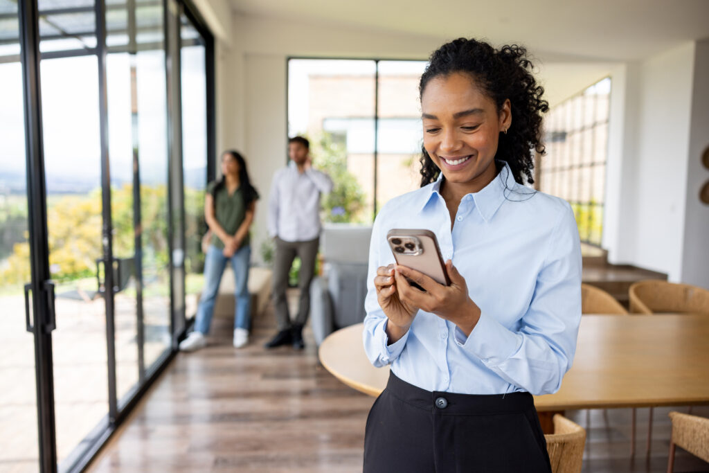 Happy real estate agent texting on her cell phone while showing a house to a couple and giving them some space