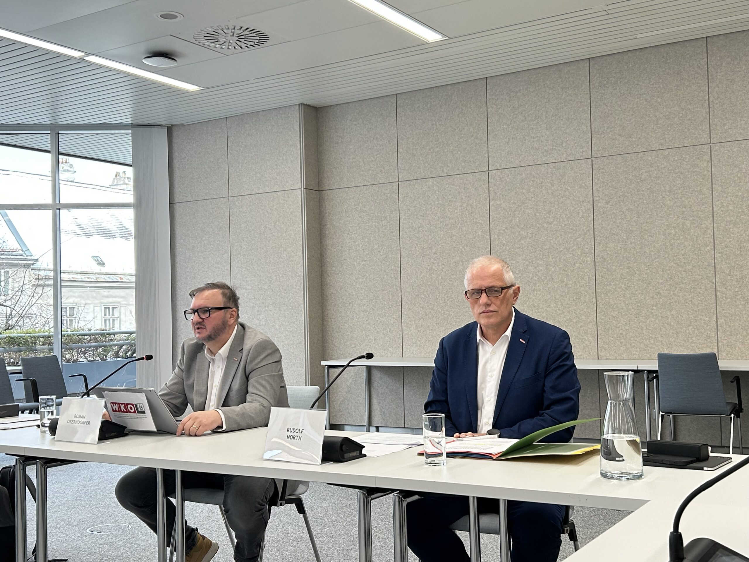 Zwei Herren bei einer Pressekonferenz, vor ihren Mikrophonen