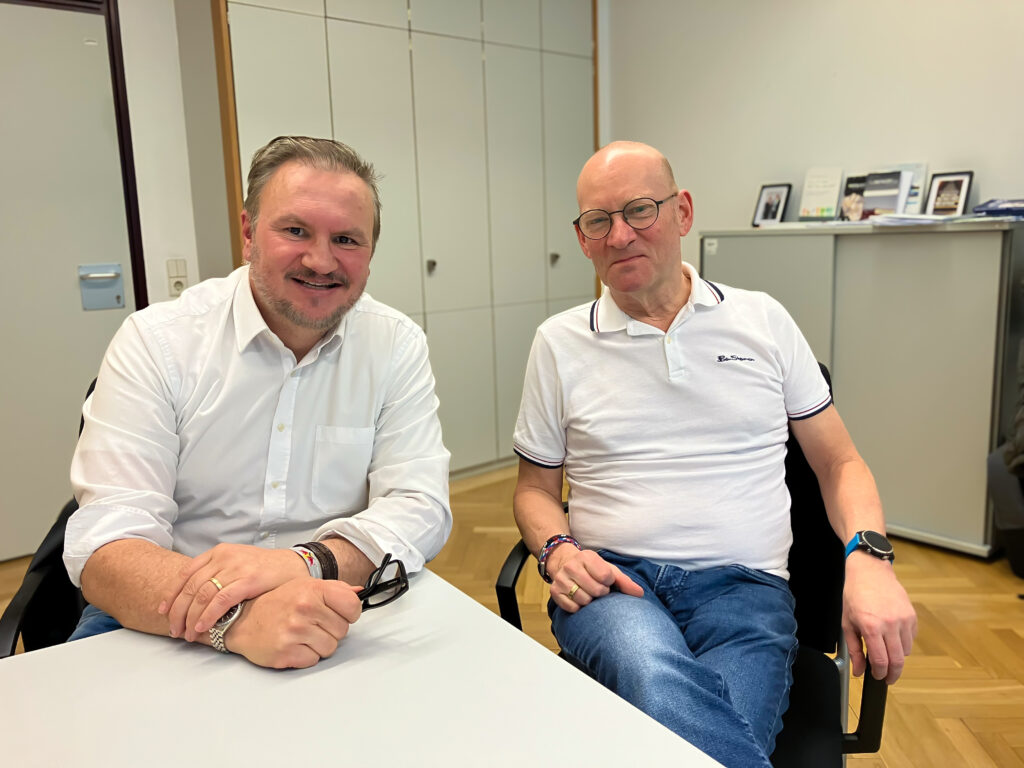 Zwei Männer in weißen Hemden nebeneinander sitzend